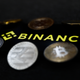 The Binance logo in front of a few random coins, some with the bitcoin symbol on them.